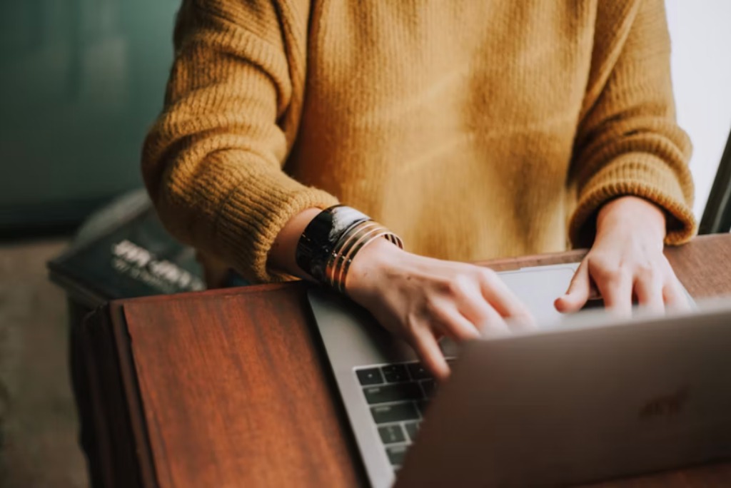woman in a gold sweater working at a desk on her laptop signaling an SEO strategy used by page seven marketing.