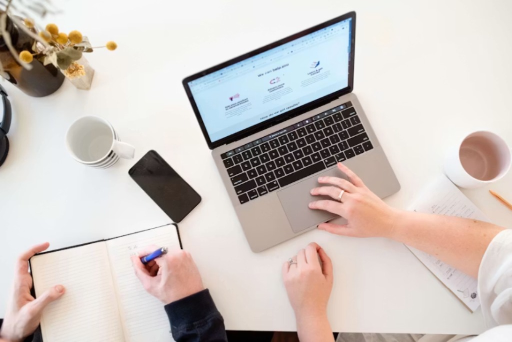 overhead desk with coffee and laptop with co-workers working on page seven marketing legal SEO for law firms.